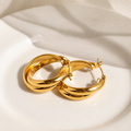 A pair of polished gold hoop earrings resting on a white ceramic plate with soft shadows cast across it.